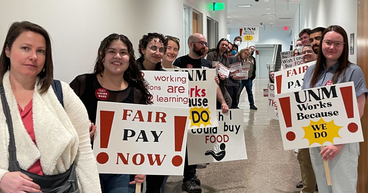 Graduate workers line a hallway with signs reading Fair Pay Now and UNM Works Because We Do