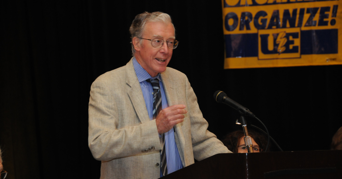 The historian David Montgomery speaking in front of a banner that says Organize! UE