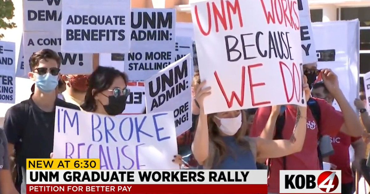 Still image of TV coverage of rally. Title reads UNM Graduate Workers Rally, Petition for Better Pay. Workers holding signs, most prominent one reads UNM Works Because We Do