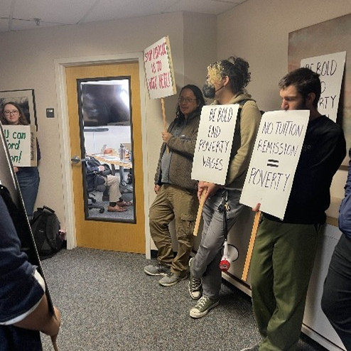 UE Loca l1498 members standing in a hallway outside a door with picket signs.