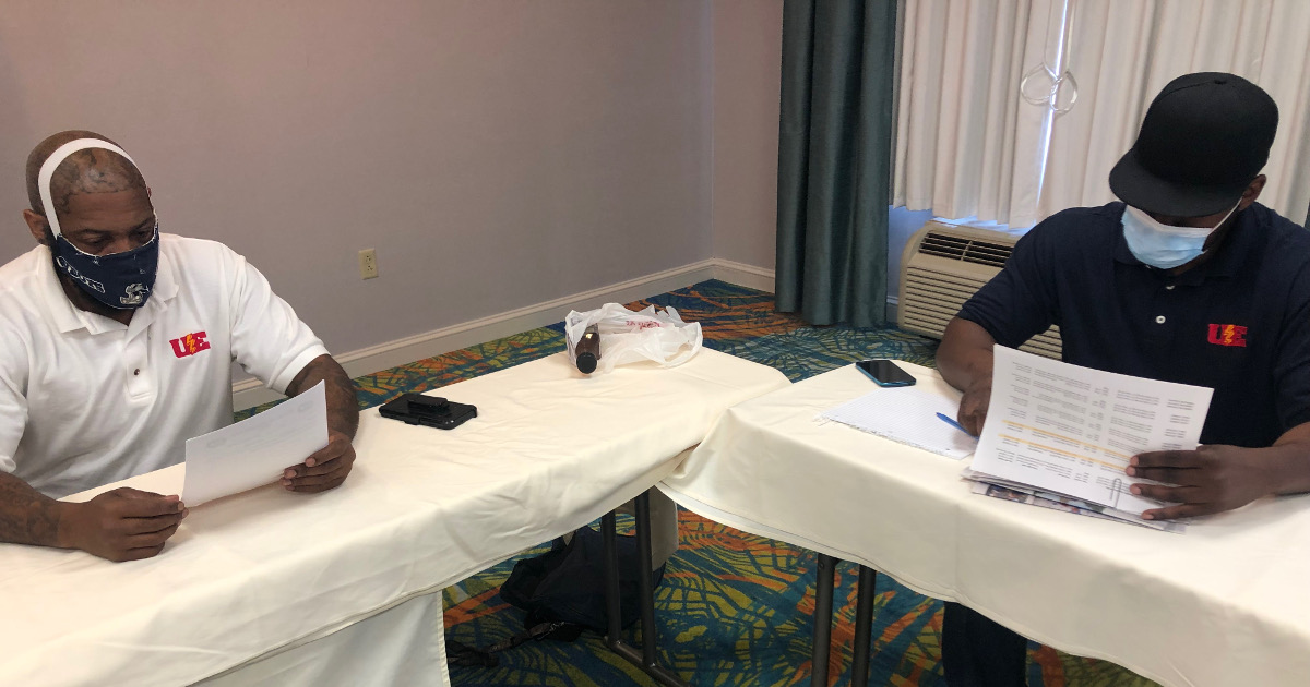 Two men wearing masks, spaced apart from each other, looking at papers at a table